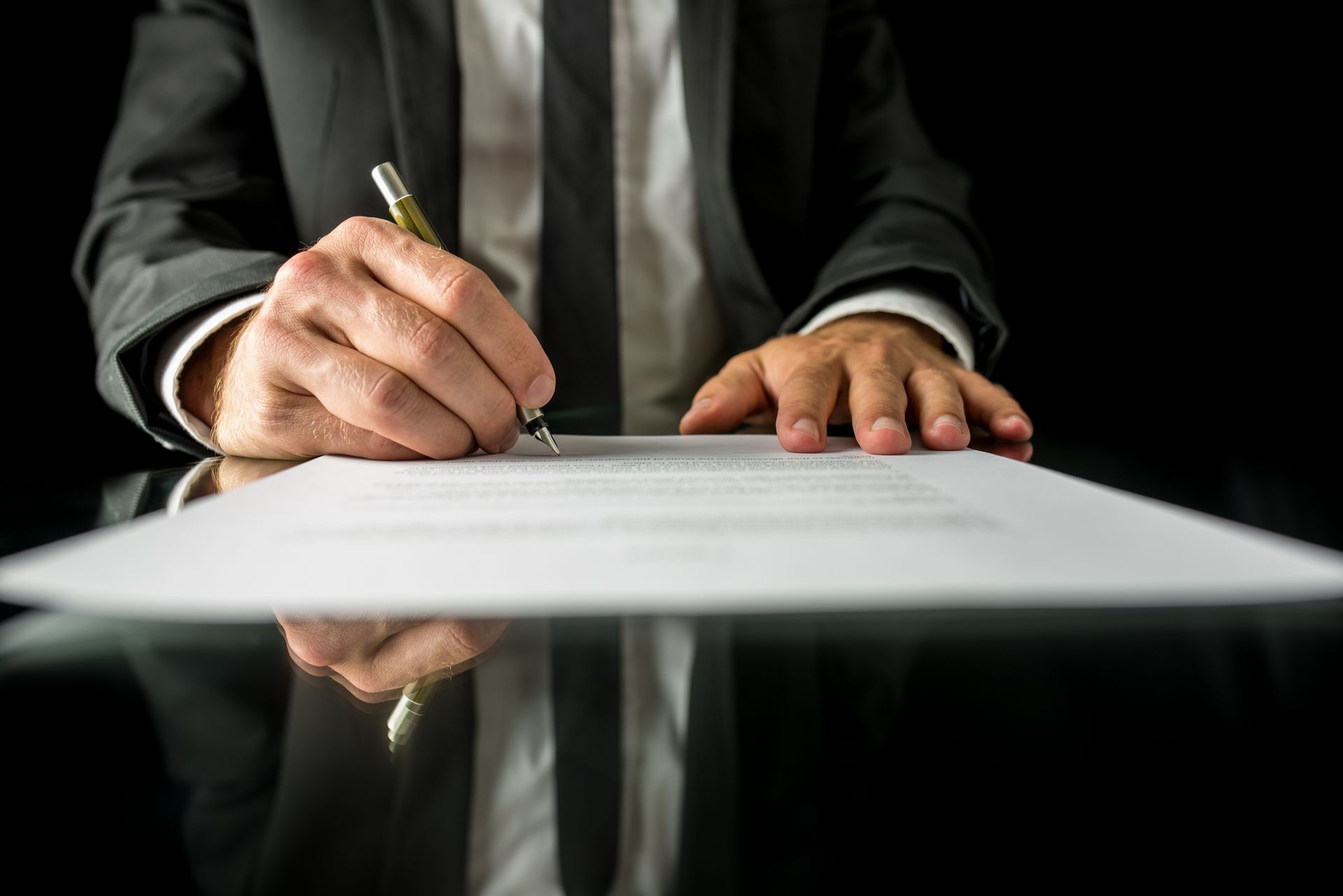 Person in a suit signing a document with a pen at a desk