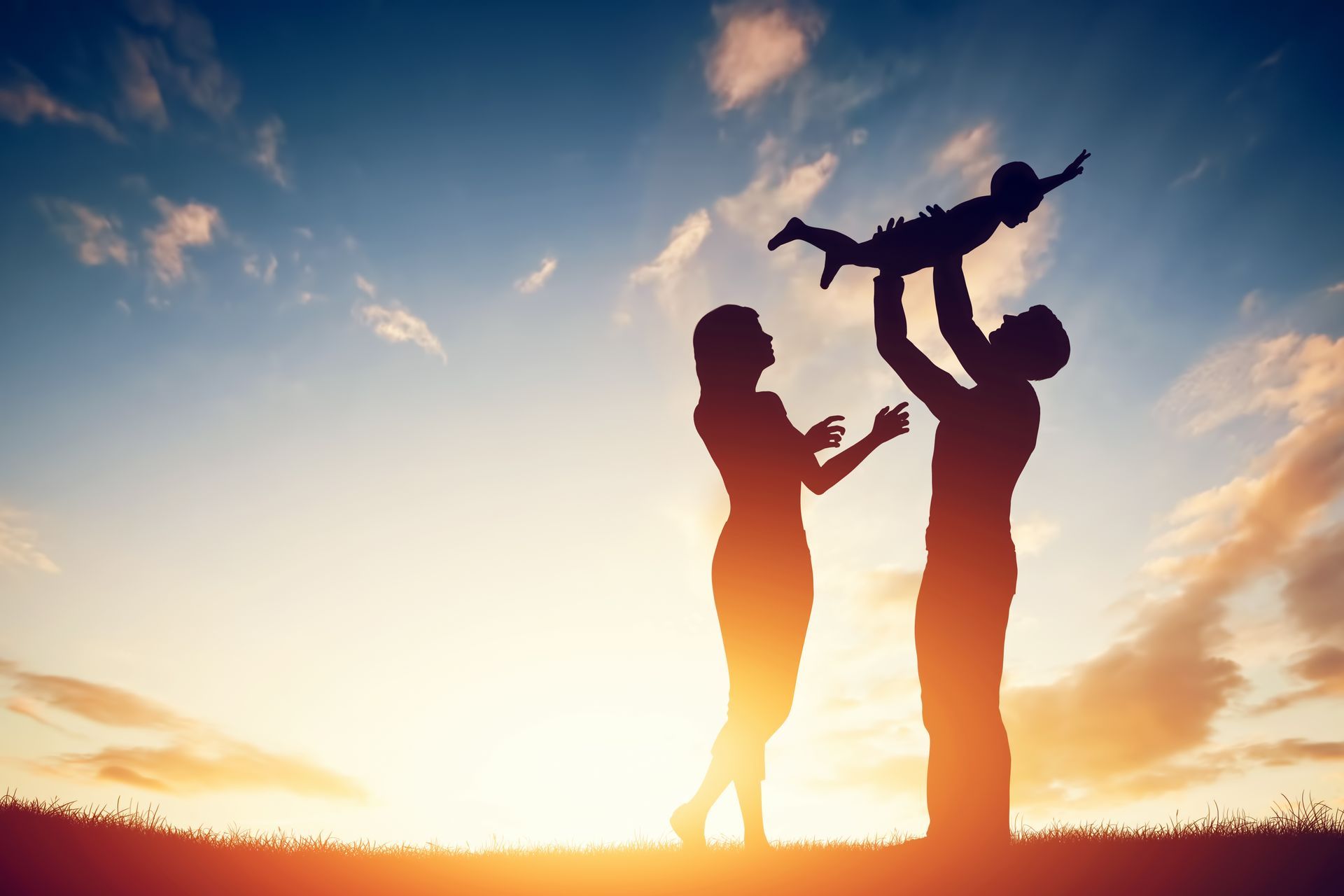 Silhouettes of two adults lifting a child overhead at sunset on a beach