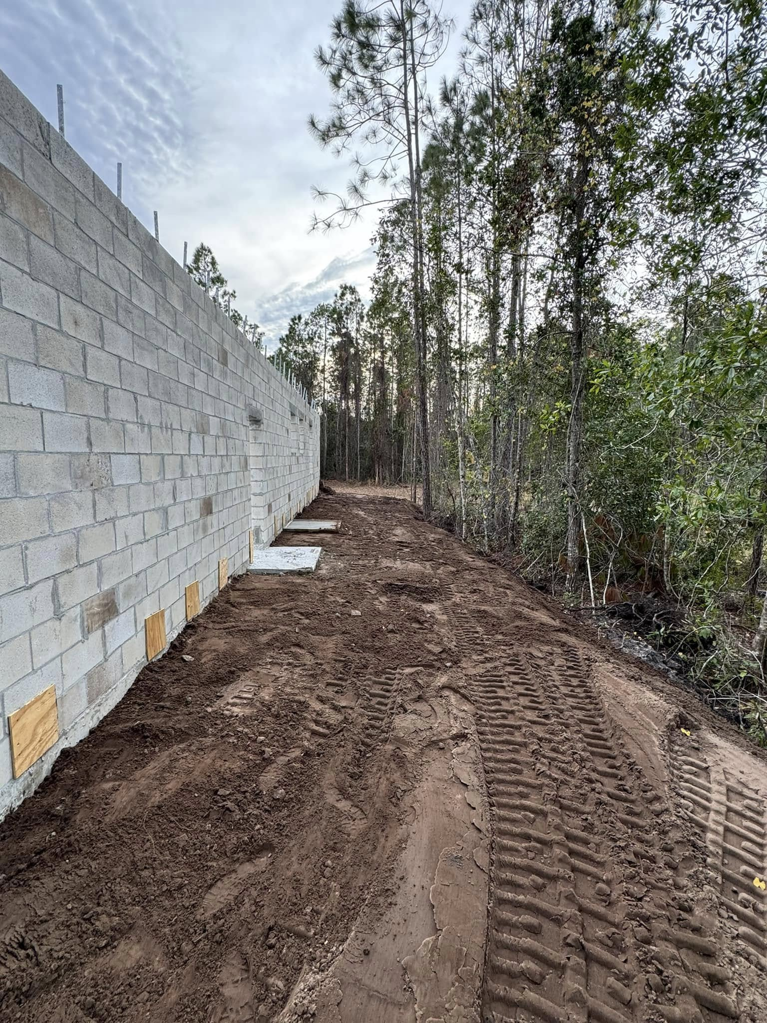 Construction site: concrete block wall next to a dirt path and trees.
