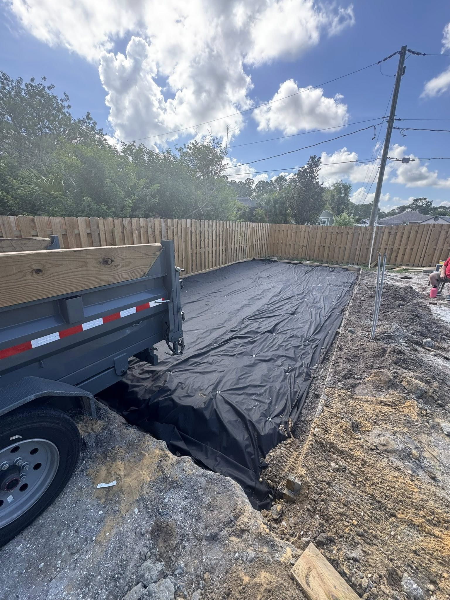 A trailer next to a construction site covered in black fabric, with a wooden fence and power lines in the background.