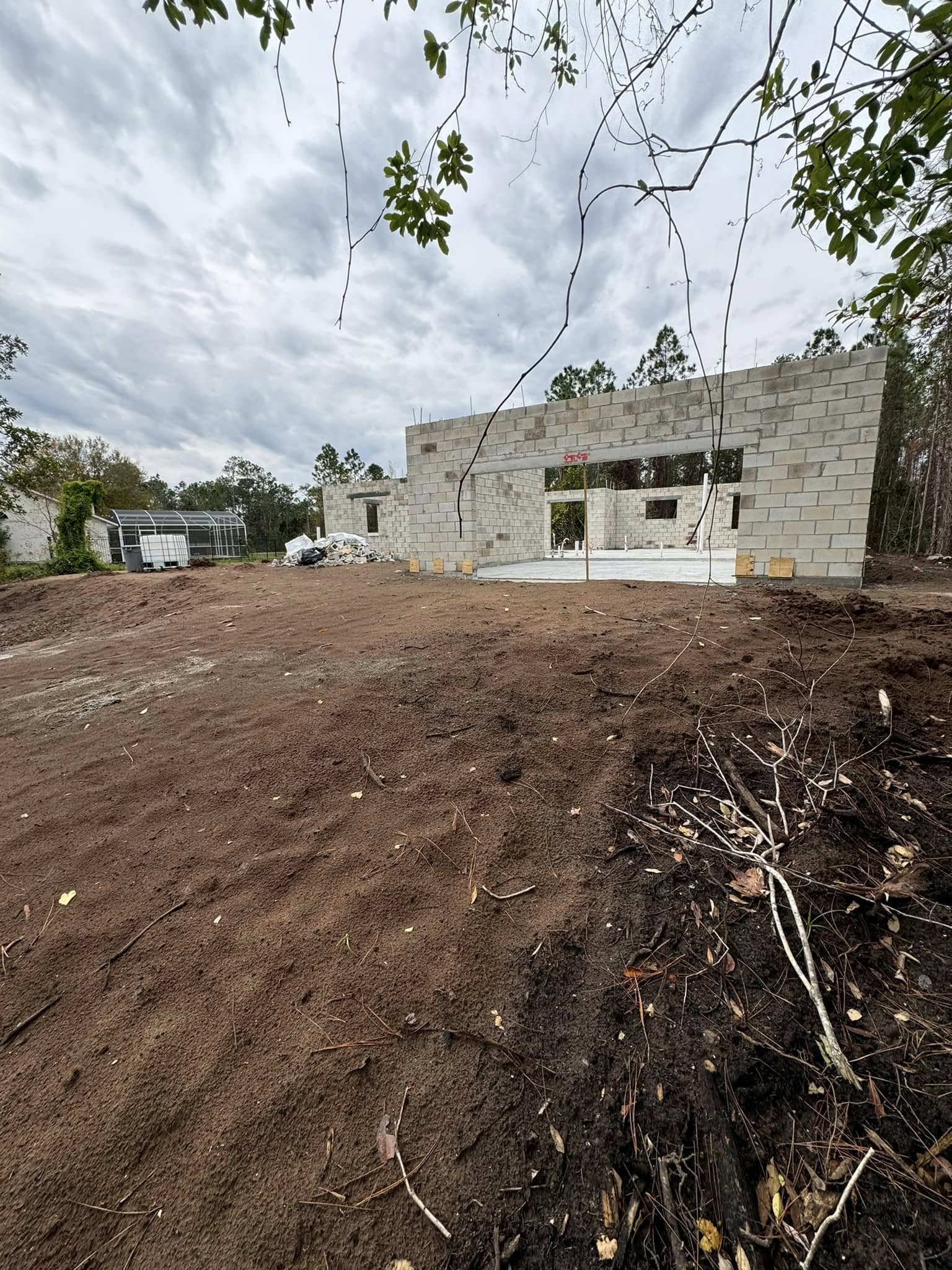 Construction site with unfinished concrete block building, dirt, and cloudy sky.
