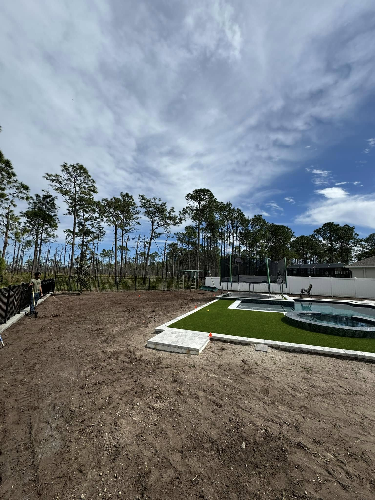 Backyard with pool, freshly seeded lawn, fence, trees, and partly cloudy sky.
