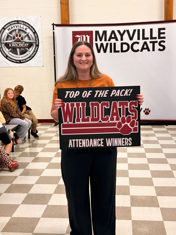 A teacher holding a sign that says Top of the Pack - Wildcats - Attendance Winners