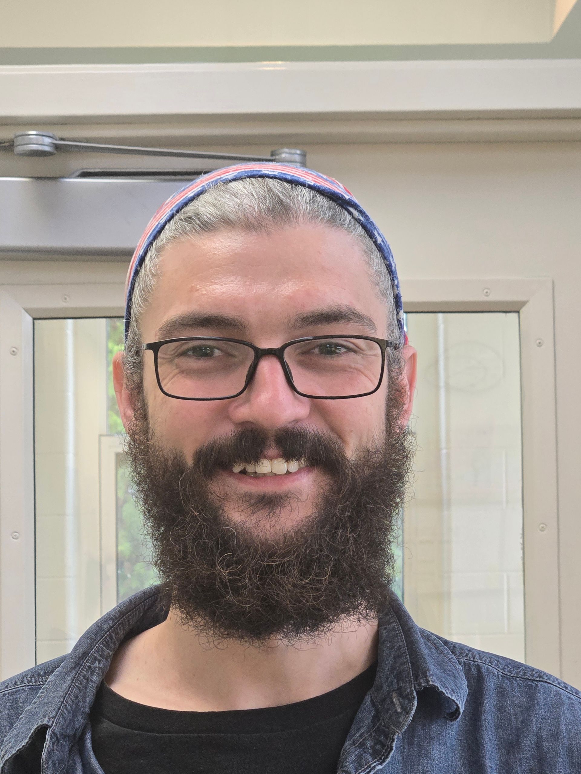 A man with a full beard and glasses smiling for the camera