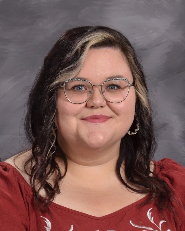 A woman wearing glasses and a red shirt is smiling for the camera.