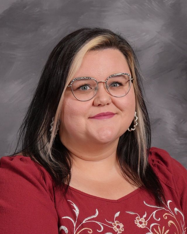 A woman wearing glasses and a red shirt is smiling for the camera.