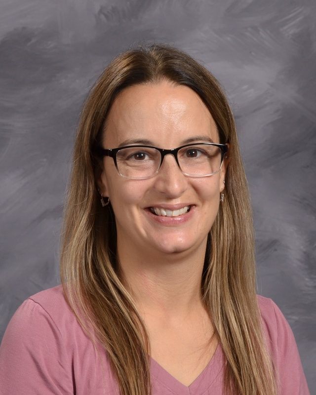 A woman with long hair wearing glasses and pink shirt smiling for the camera