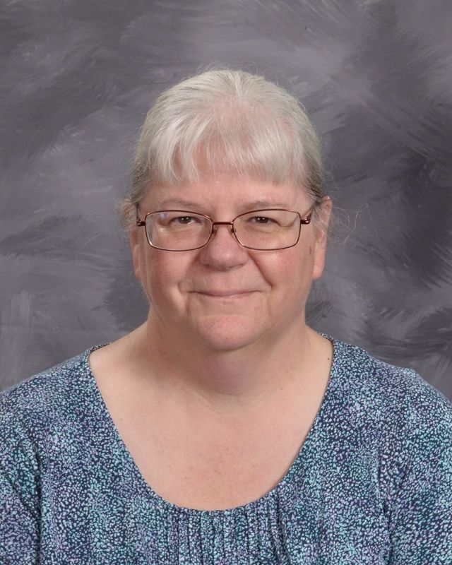 A woman wearing glasses and a blue shirt smiles for the camera