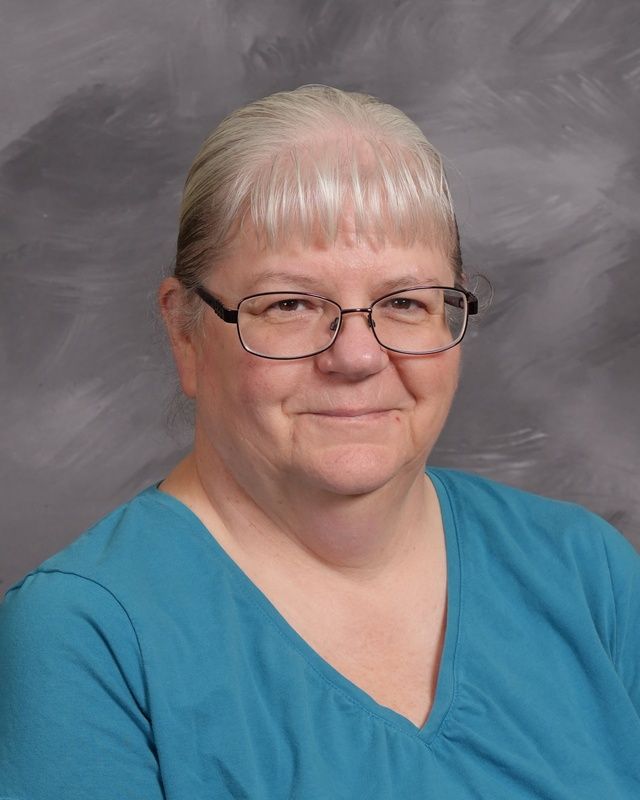 A woman wearing glasses and a blue shirt smiles for the camera