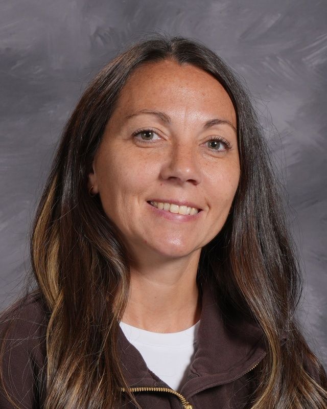 A woman with long brown hair is smiling in front of a grey background.