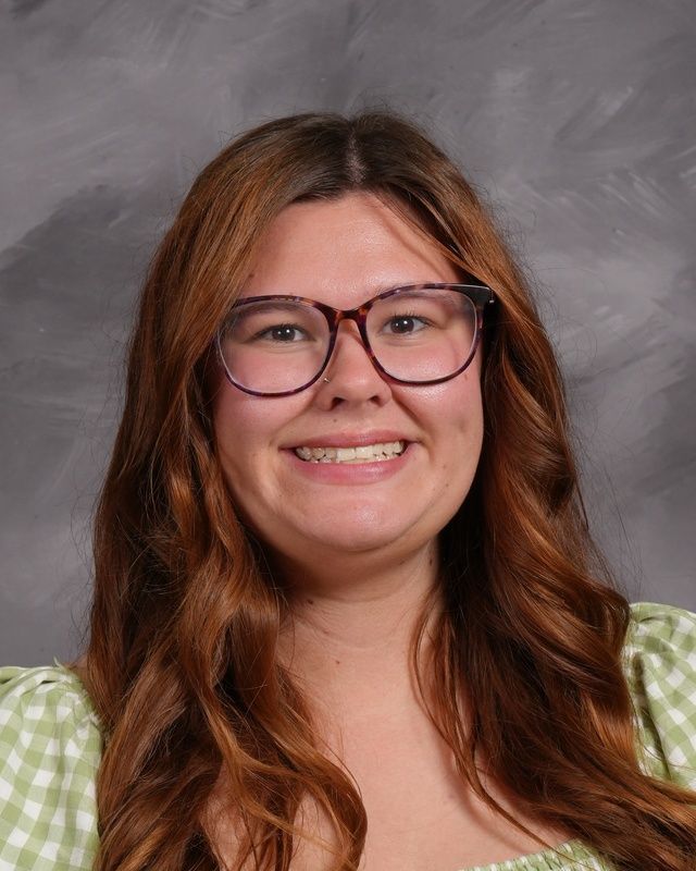 A woman with long hear wearing glasses and a grey stiped shirt smiling for camera