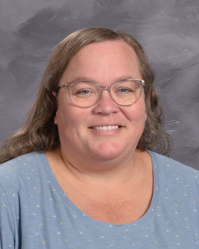 A woman wearing glasses and a grey shirt is smiling for the camera.