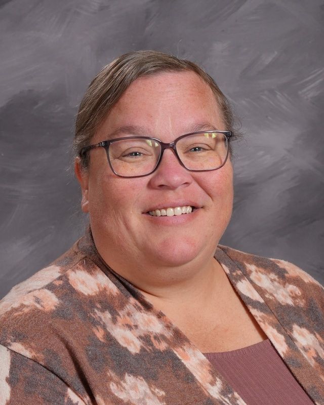 A woman wearing glasses and a grey shirt is smiling for the camera.