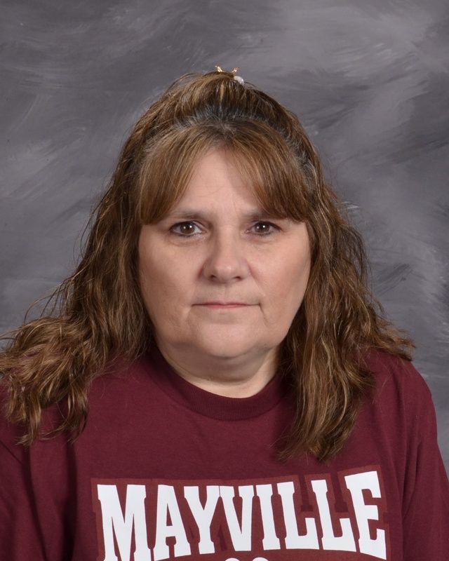 A woman with long hair wearing a maroon Mayville shirt posing for the camera