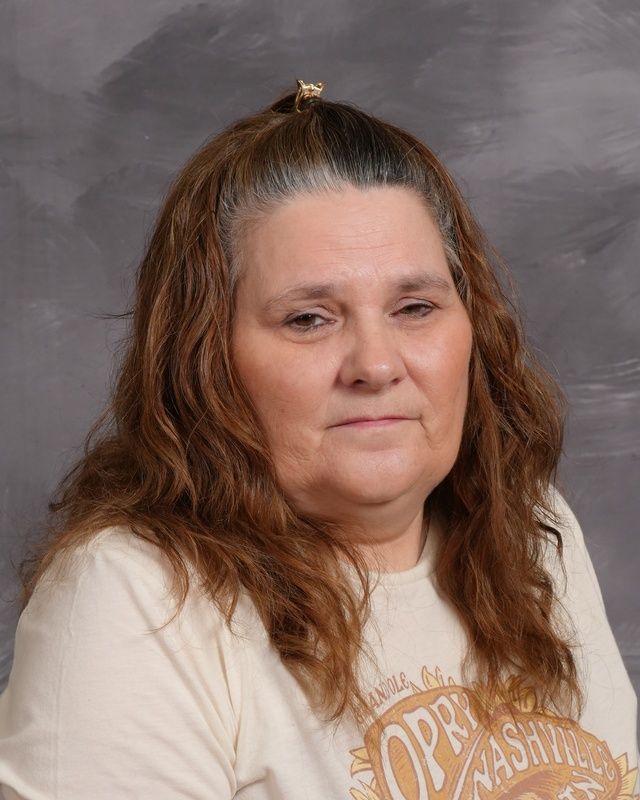 A woman with long hair wearing a maroon Mayville shirt posing for the camera