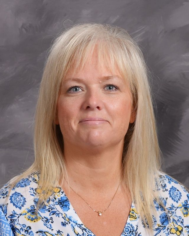 A woman with blonde hair is smiling in front of a grey background.