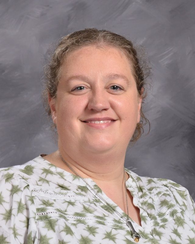 A woman wis smiling for the camera in front of a grey background.