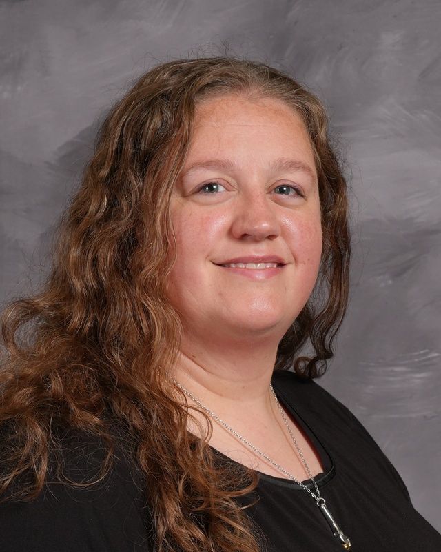 A woman wis smiling for the camera in front of a grey background.