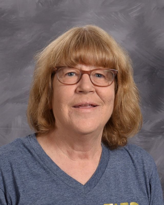 A woman wearing glasses and grey shirt smiling for the camera