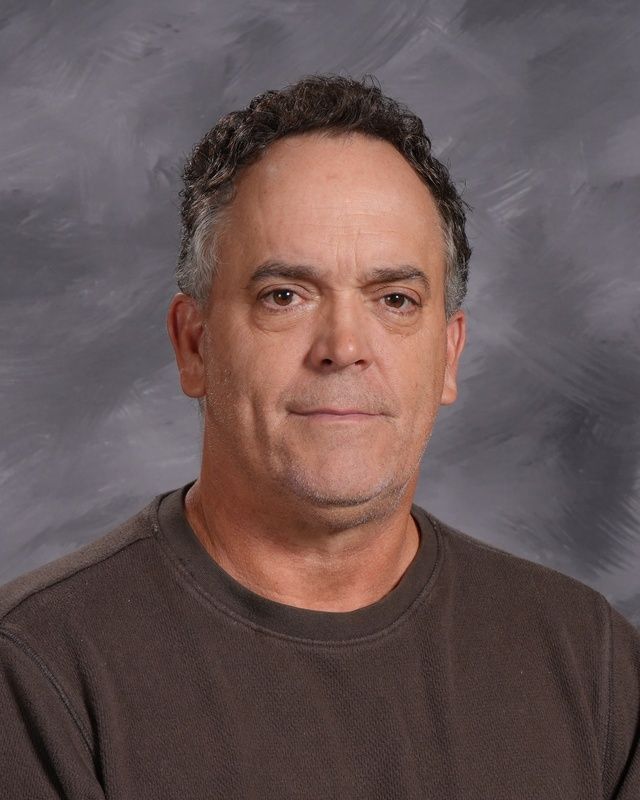 A man in a dark grey shirt is smiling for the camera