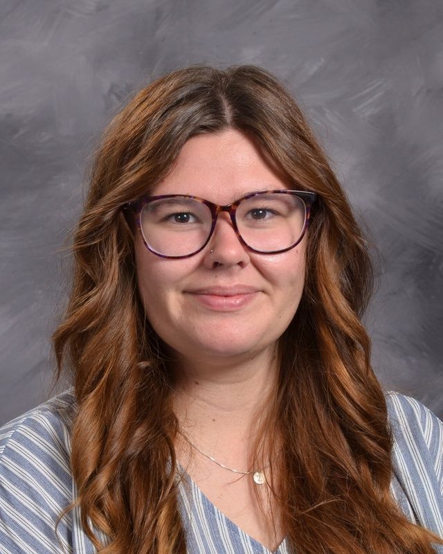 A woman with long hear wearing glasses and a grey stiped shirt smiling for camera