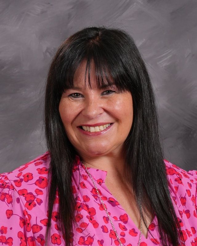 A woman wearing a white shirt and earrings smiles for the camera