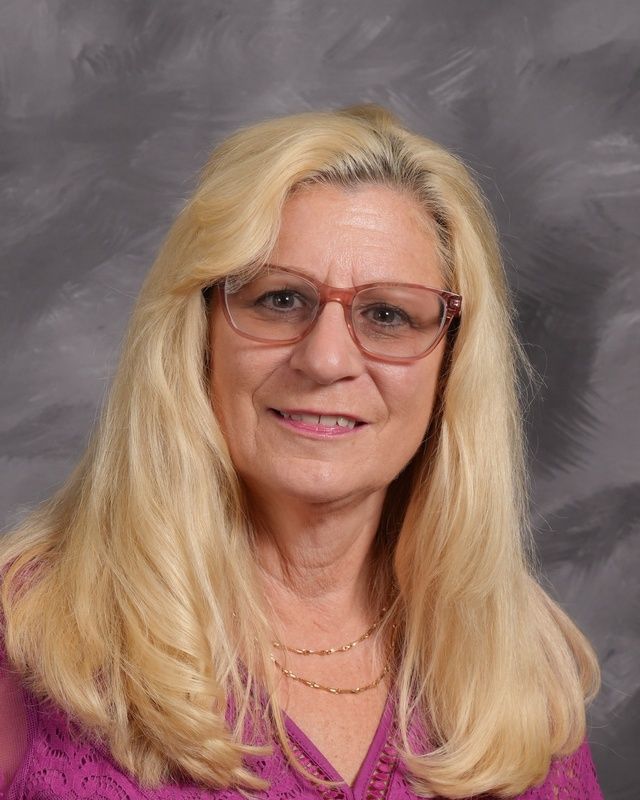 A woman with long blonde  hair wearing glasses and a black shirt smiles for the camera