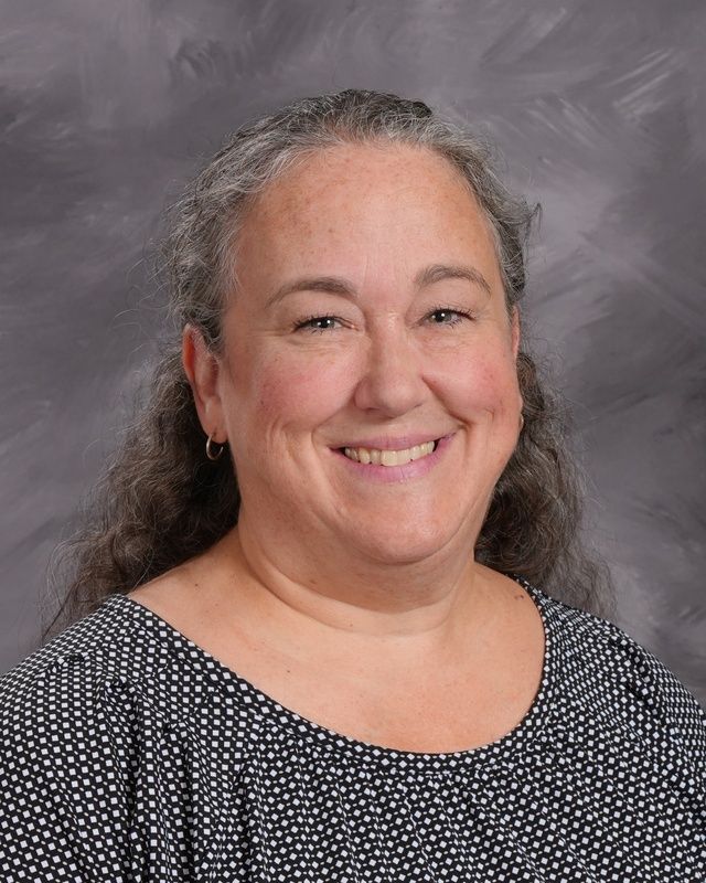 A woman in a dark shirt is smiling for the camera.