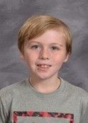A young boy in a Grey t-shirt smiling for the camera