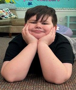 A young boy resting his head on his hands smiling for the camera