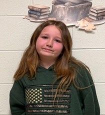 A young girl with long hair wearing a green sweatshirt with the US flag on it smiling for the camera