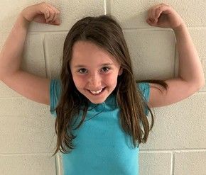 A girl with long hair showing her bicep muscles smiling for the camera