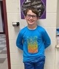 A young boy wearing glasses and a blue long sleeve shirt smiling for the camera