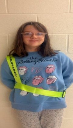 A young girl wearing a rolling stones sweatshirt and a safety patrol badge smiling for the camera