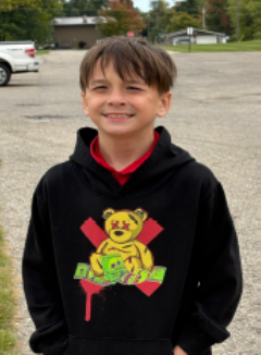 A young boy with dark hair wearing a black hoodie smiling for the camera