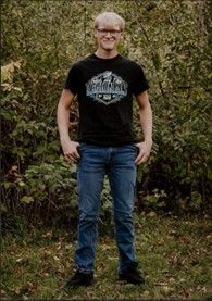 A young man wearing a black shirt and jeans standing outside smiling for the camera