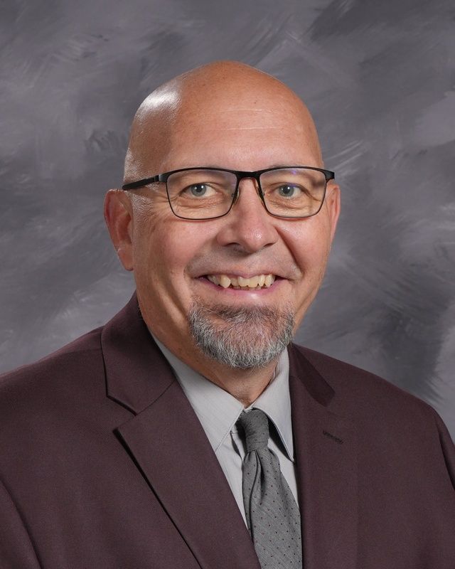 Man wearing pink suit with red shirt and glasses smiling