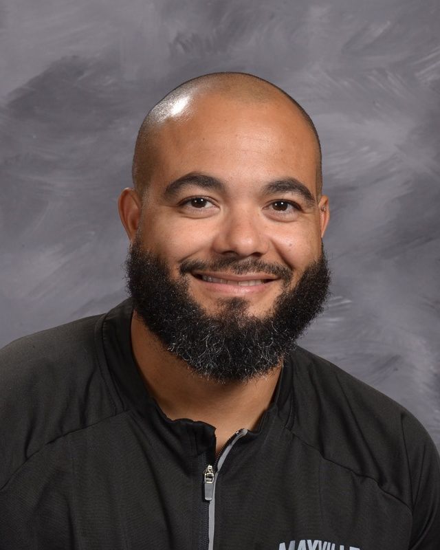 A man with a beard is wearing a blue shirt smiling for the camera