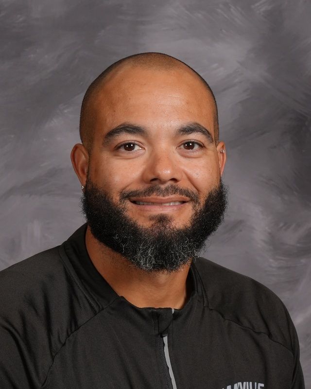 A man with a beard is wearing a blue shirt smiling for the camera