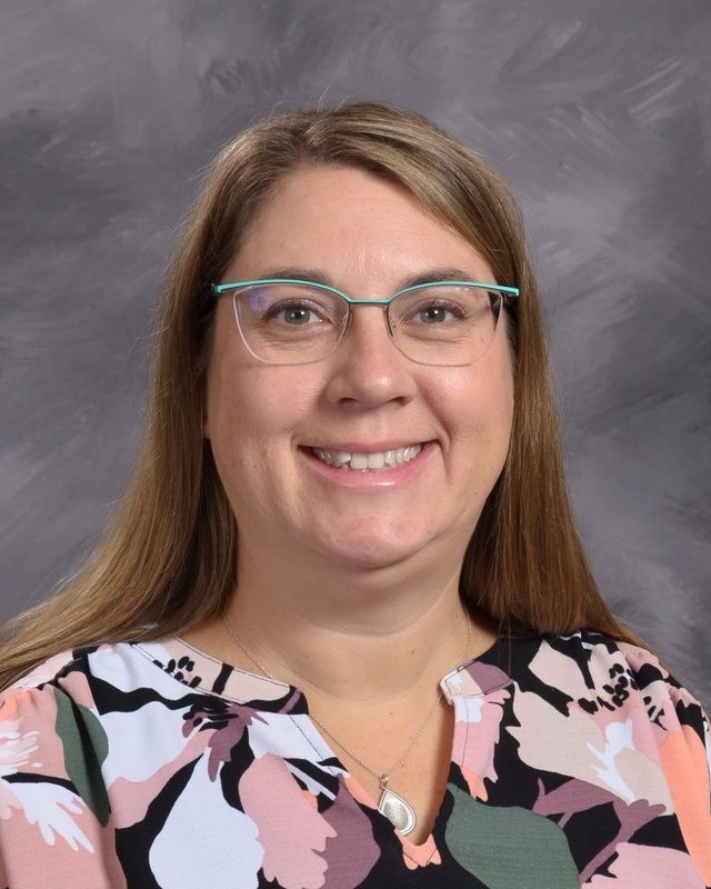A woman wearing glasses and a pink & white shirt smiles for the camera