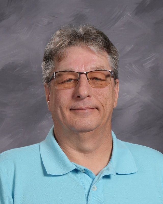 Man in glasses and wearing a purple shirt grinning for the camera