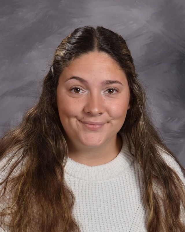 A woman with long hair and wearing a white sweater smiling for the camera