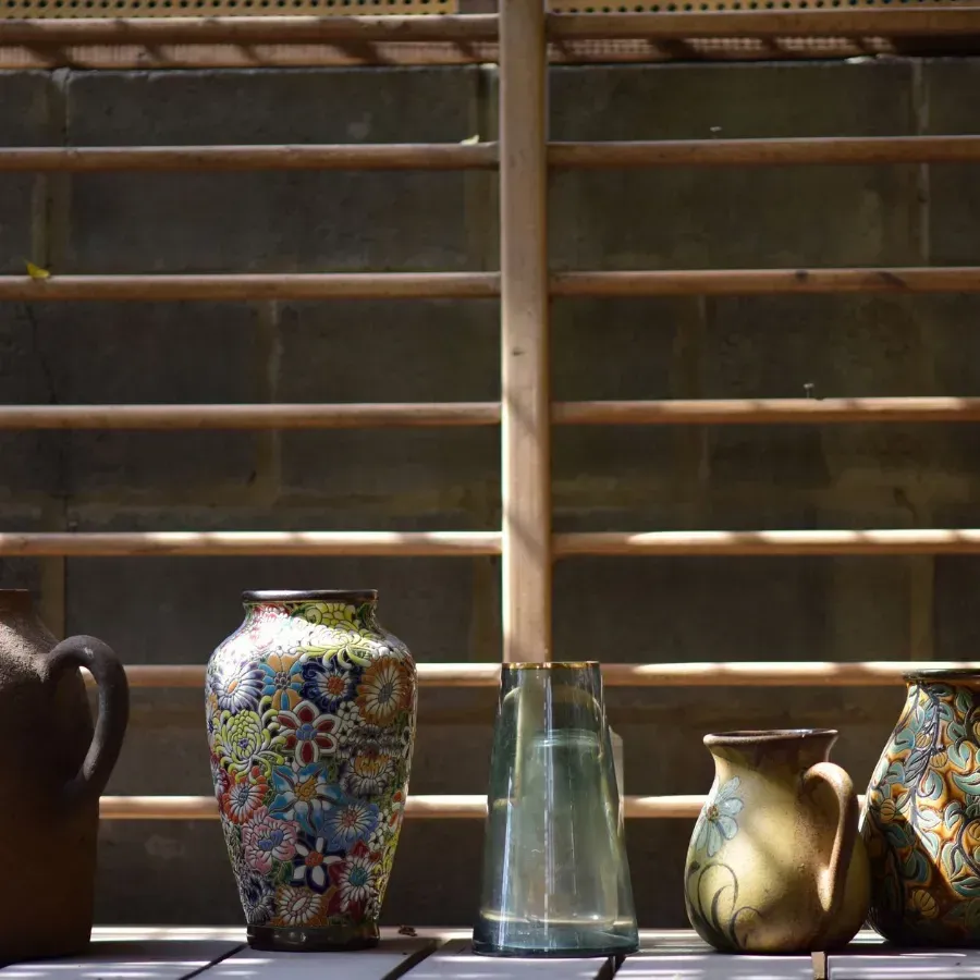 Wooden bookshelf with books and decor, topped with vases, flowers, and a lamp against a pale green wall