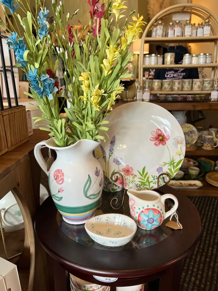 Decorative porcelain vase with flowers, plates, and teacup on a wooden table in a shop display