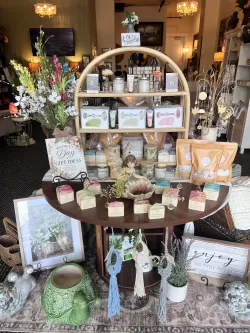 Decorated shop display with flowers, candles, gifts, and home décor on a round table and shelves