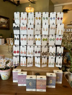 Jewelry display with rows of earrings on cards and small perfume bottles on a wooden table in a boutique.