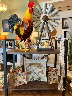 Colorful rooster sculpture on a rustic table, with pillows and a windmill decor in a cozy room