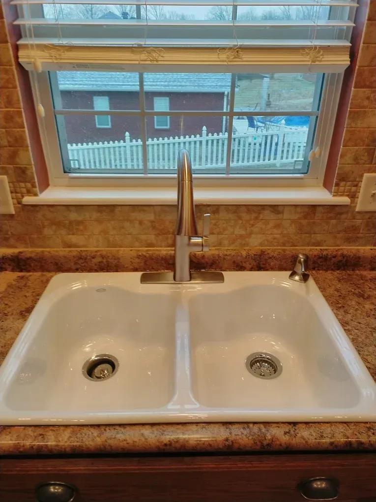 Double kitchen sink beneath a window, with a chrome faucet and granite countertop.
