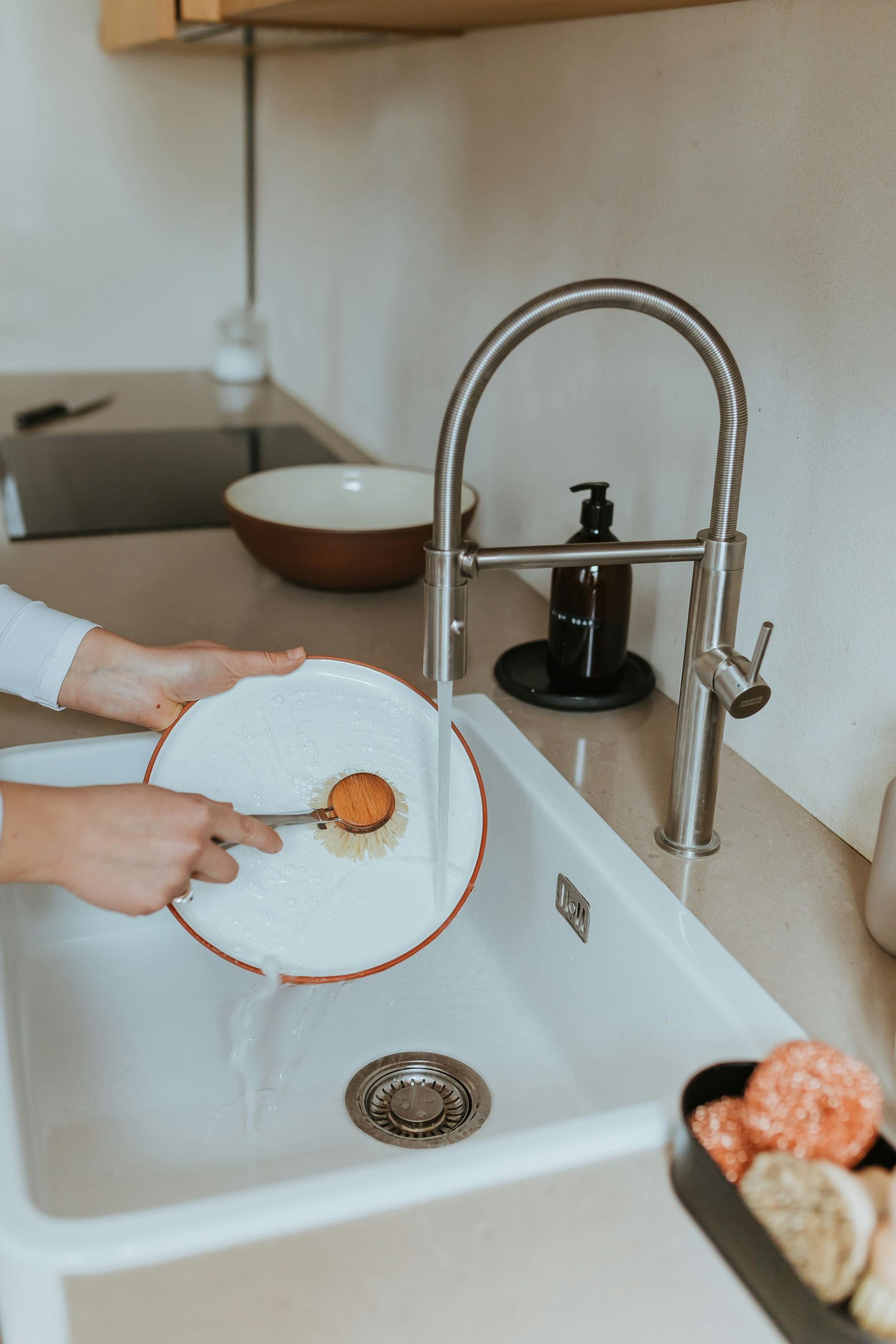 Hands washing a white plate in a kitchen sink with running water
