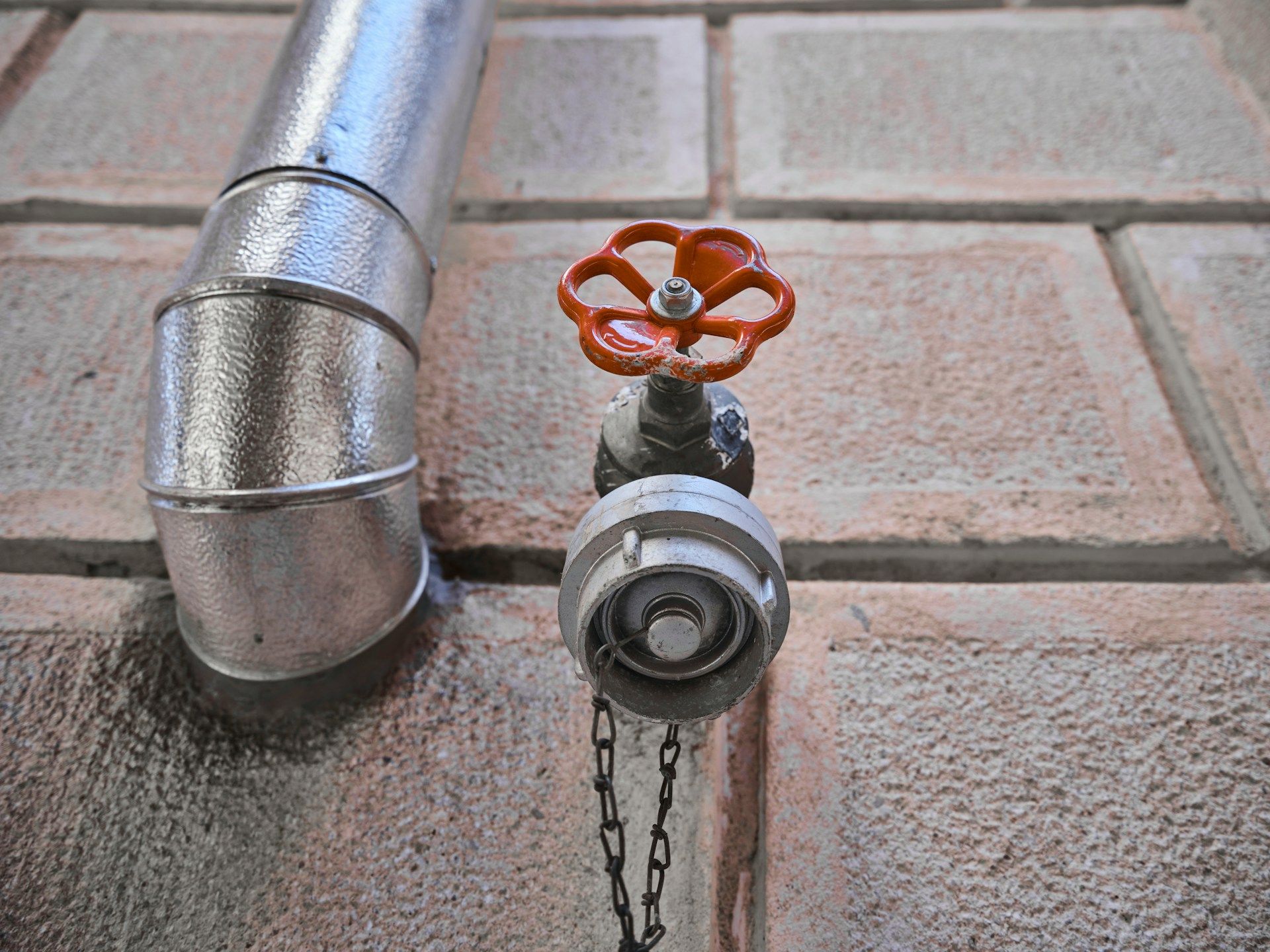 Metal pipe with a red valve on a tiled floor, with a chain hanging from the valve.